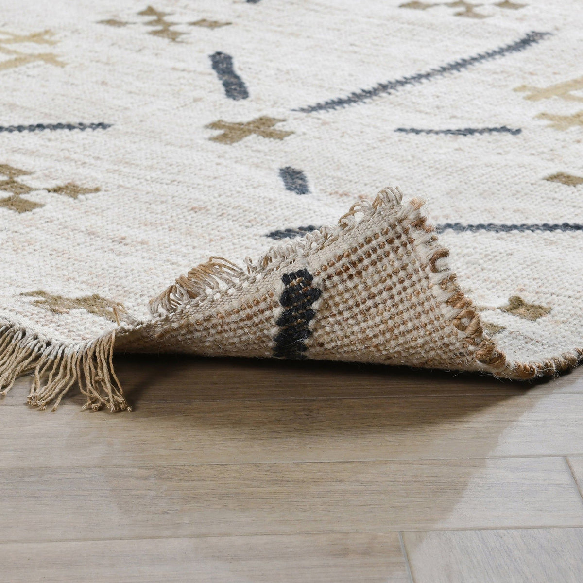 Ivory area rug with dark blue and tan geometric motifs, corner fold and fringe