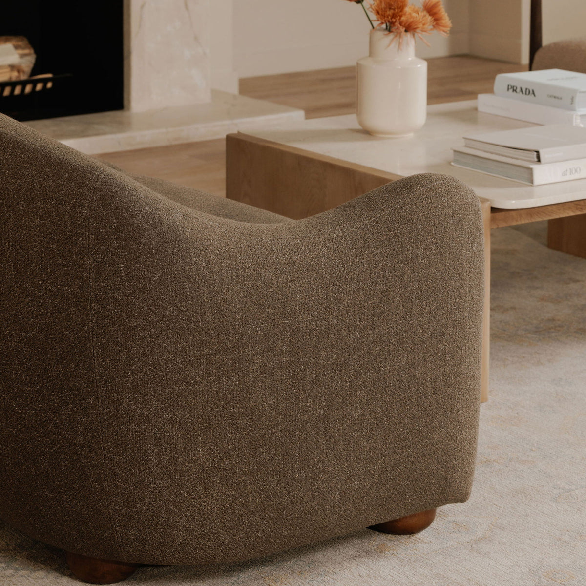 Close-up of the brown sofa's textured upholstery, rounded arm, and wooden feet