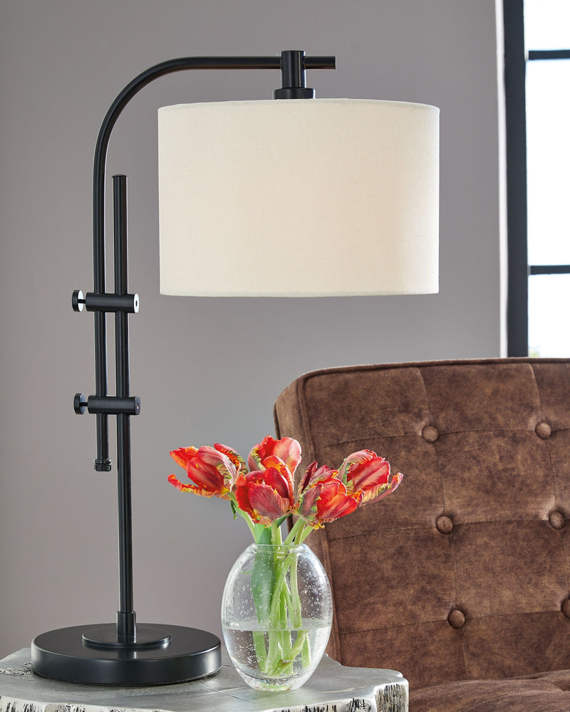 Black metal lamp with curved arm, cream drum shade, and round pedestal base.
