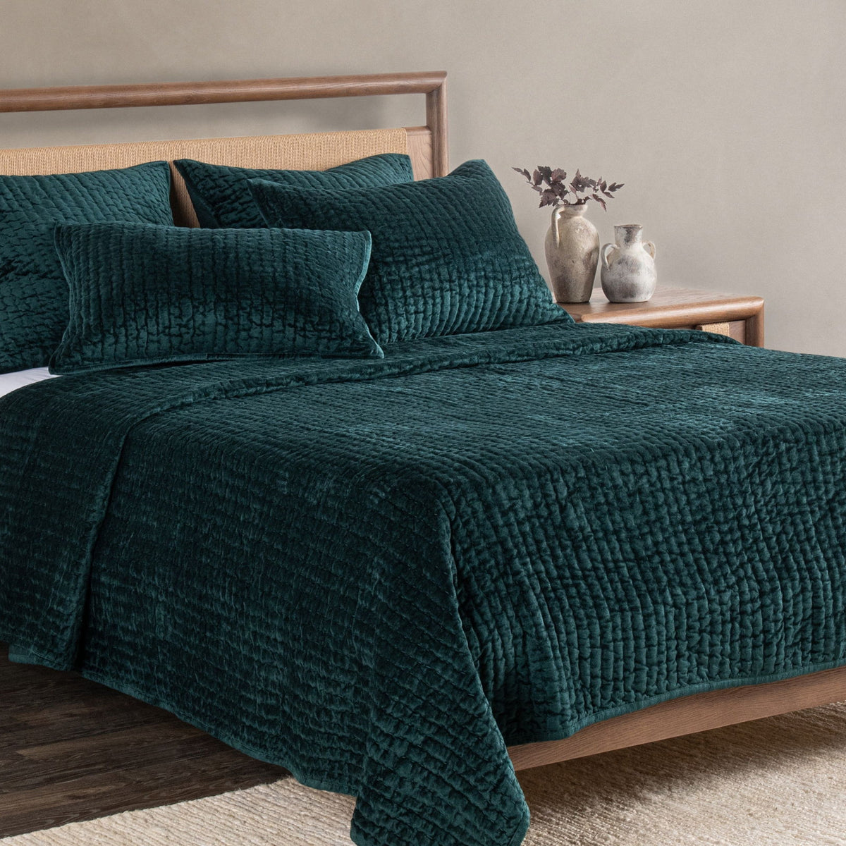Emerald velvet quilt set with textured square pillows on bed