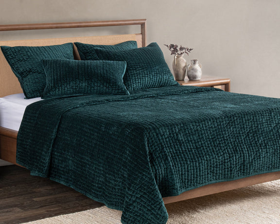 Emerald velvet quilt set with textured square pillows on bed