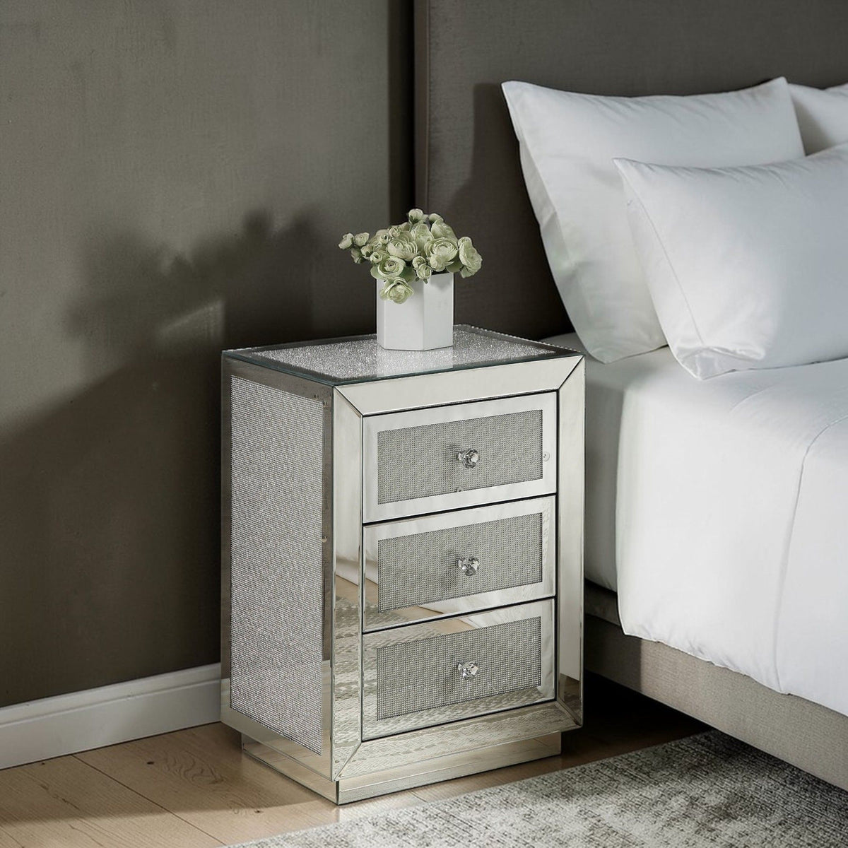 Silver mirrored nightstand with three drawers and grey textured fronts beside a sofa.