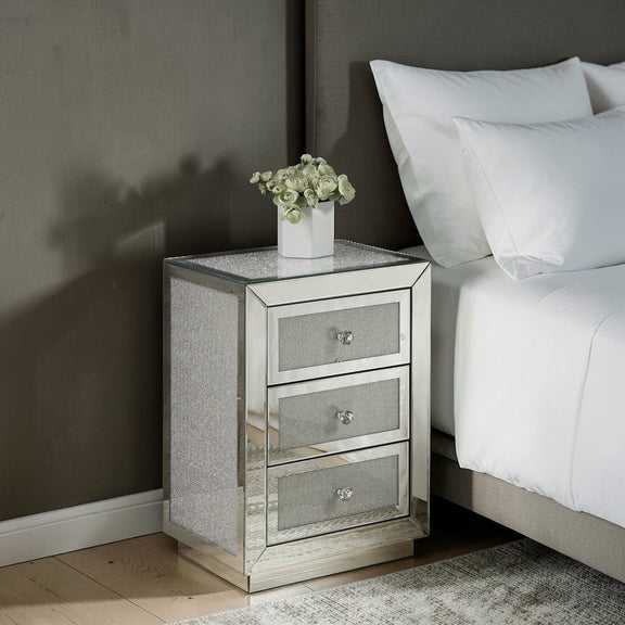 Silver mirrored nightstand with three drawers and grey textured fronts beside a sofa.