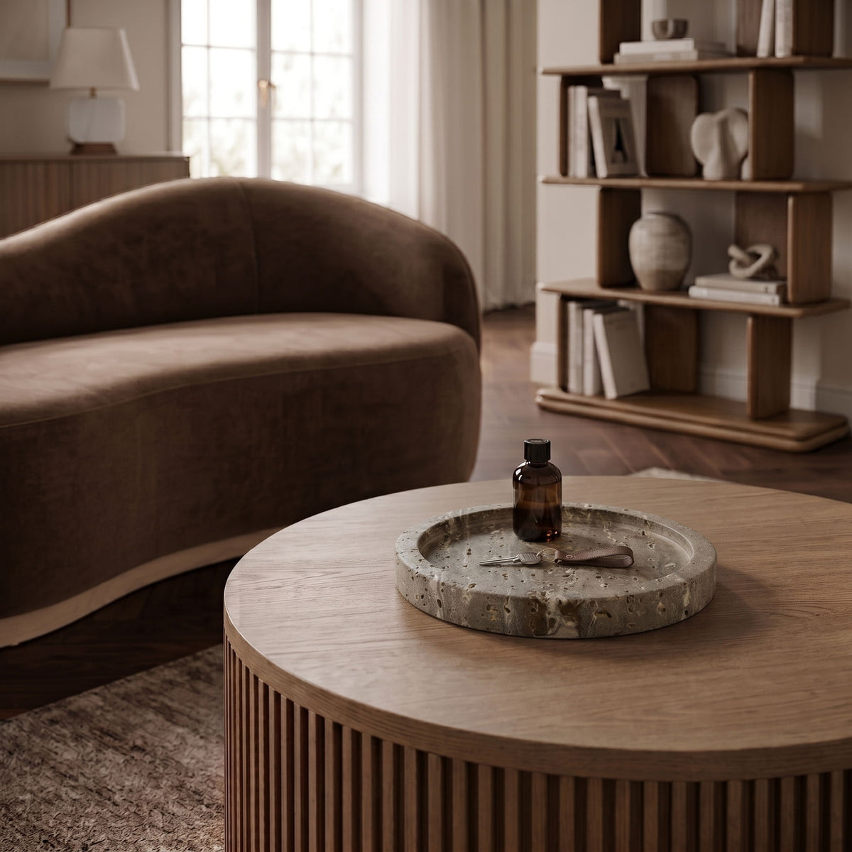 Beige travertine round tray on a table with a small bottle at center.