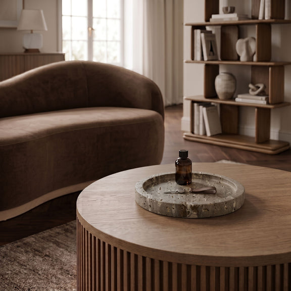 Beige travertine round tray on a table with a small bottle at center.