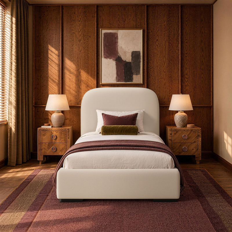 Beige upholstered bed with rounded headboard and layered bedding in a warm bedroom setting