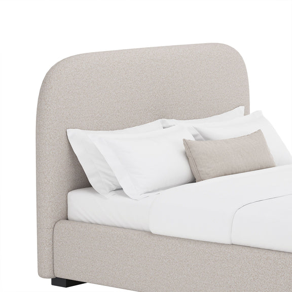 Beige upholstered bed detail with rounded headboard, white bedding, and two throw pillows