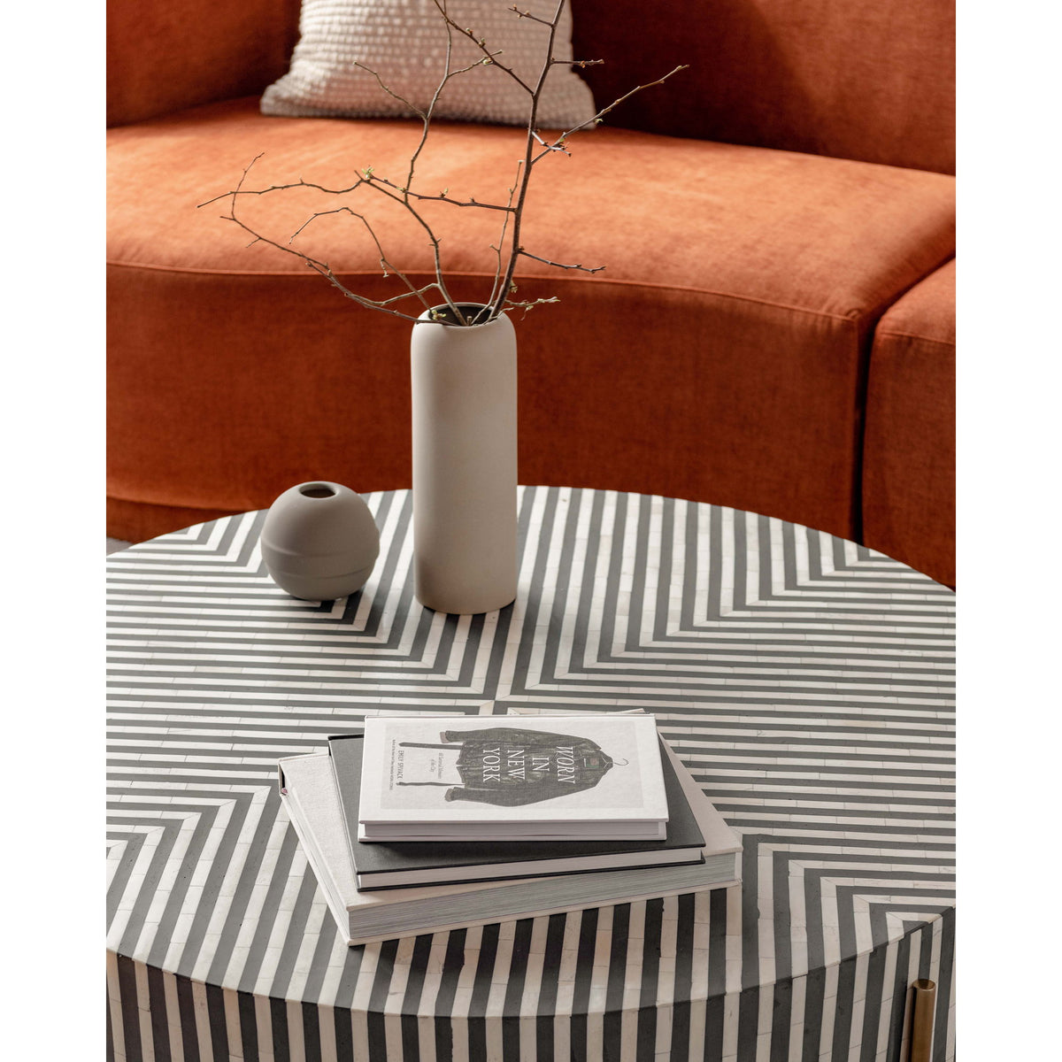 Round coffee table with striped top, vase and books on the surface