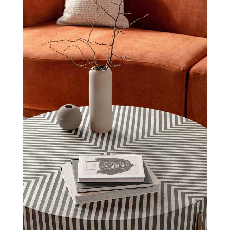 Round coffee table with striped top, vase and books on the surface
