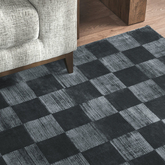 Textured black and gray check rug shown on the floor beside a light sofa