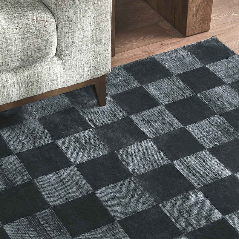 Textured black and gray check rug shown on the floor beside a light sofa