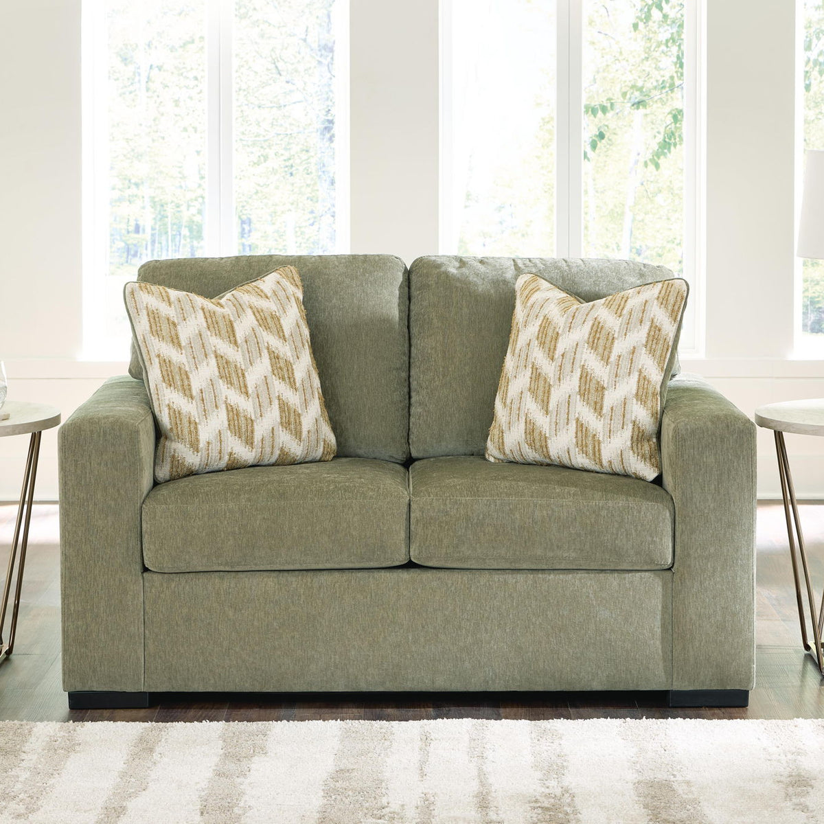Green loveseat with two patterned throw pillows and black base legs