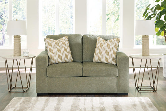 Green loveseat with two patterned throw pillows and black base legs