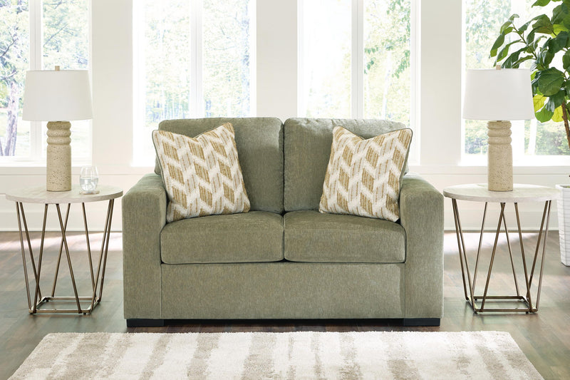 Green loveseat with two patterned throw pillows and black base legs