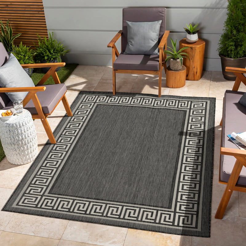 Indoor/outdoor area rug in dark gray with Greek key border pattern outdoors