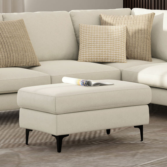 Cream upholstered ottoman with black legs in front of a sofa.
