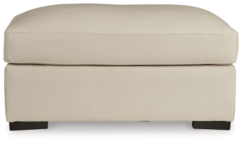 Almond ottoman with smooth padded top, stitched trim, and dark legs