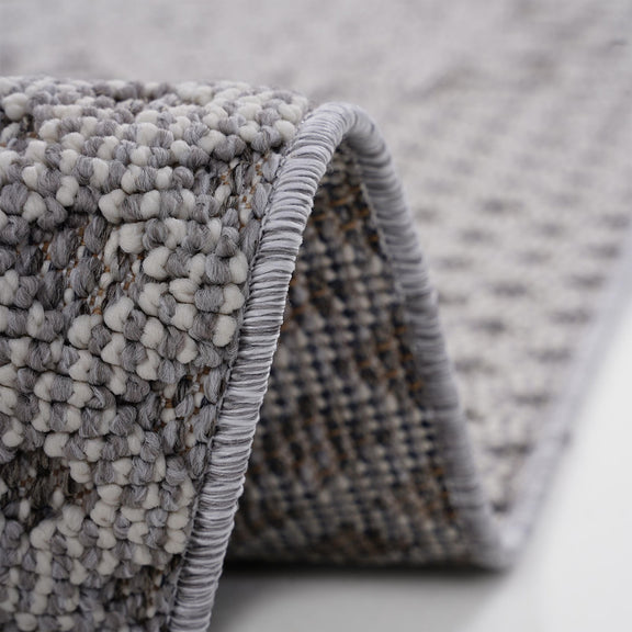 Gray rug edge with braided binding and fringe loops, close-up detail