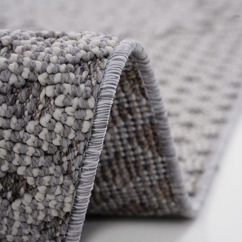 Gray rug edge with braided binding and fringe loops, close-up detail