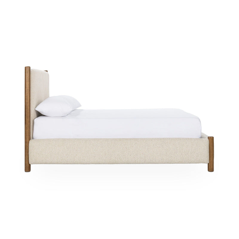 Beige upholstered bed in side view with padded headboard and wood support legs