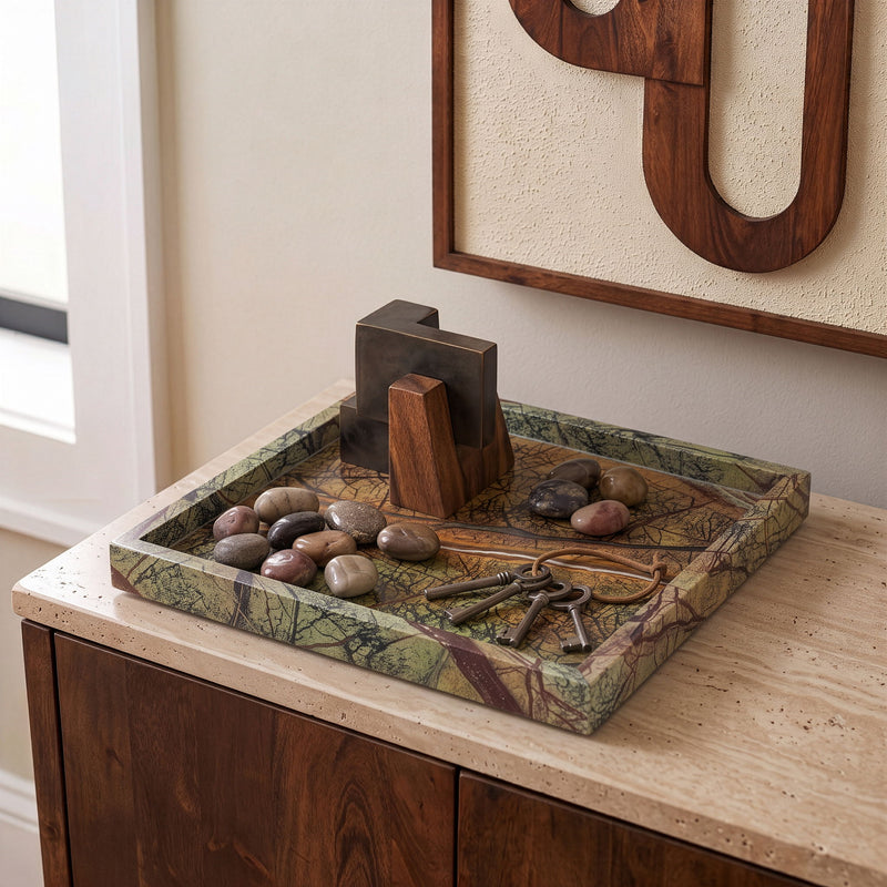 Green marble tray on dresser with metal keys and stones arranged inside.