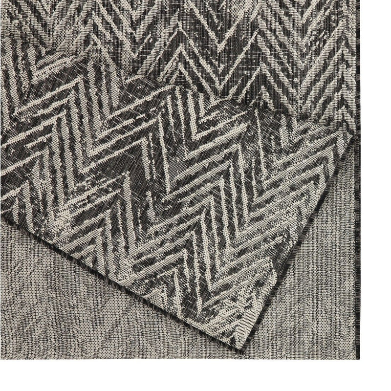 Indoor/outdoor area rug close-up: dark gray and cream chevron pattern along folded edge.