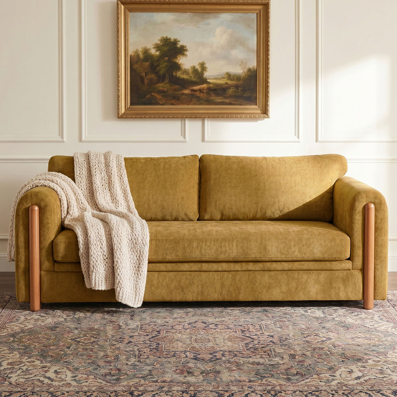 Tan 3-seat upholstered couch with wooden arms, back cushions, and knitted throw
