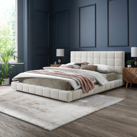 Beige upholstered bed with tufted headboard and neatly made striped blanket