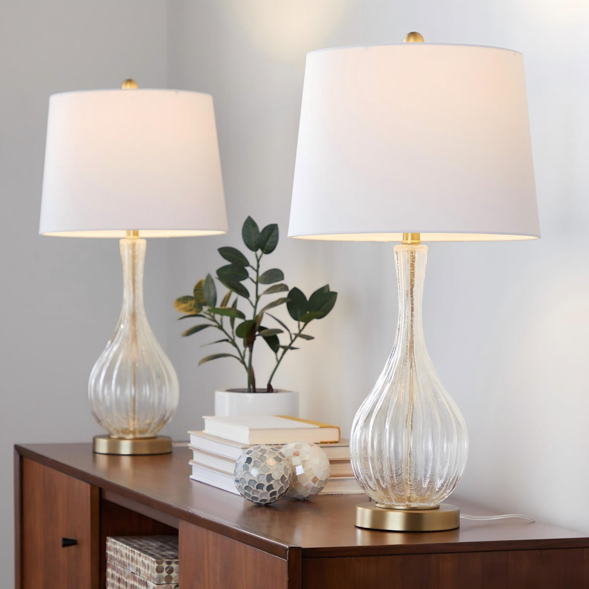 Set of 2 table lamps with white shades and clear glass urn bases, gold-toned accents.