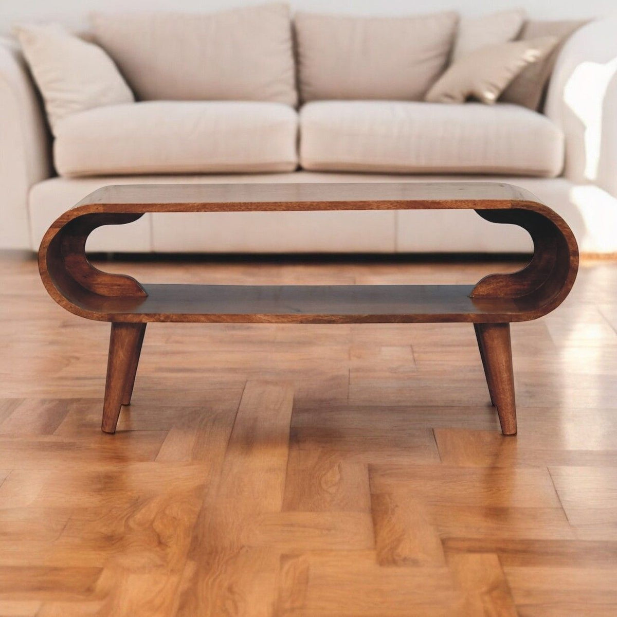 Light brown oval coffee table with sculpted cutout apron and tapered legs