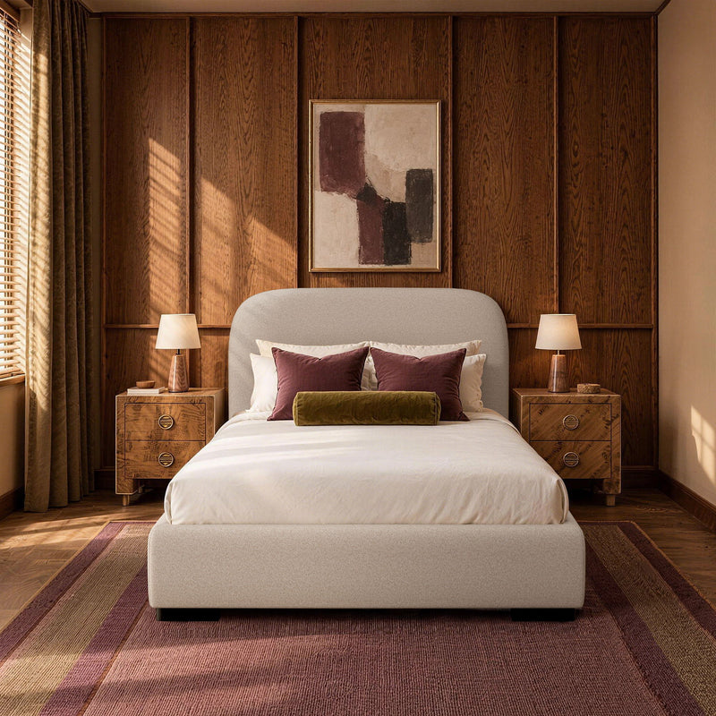 Beige upholstered bed with rounded headboard, pillows, and folded blanket on the bed