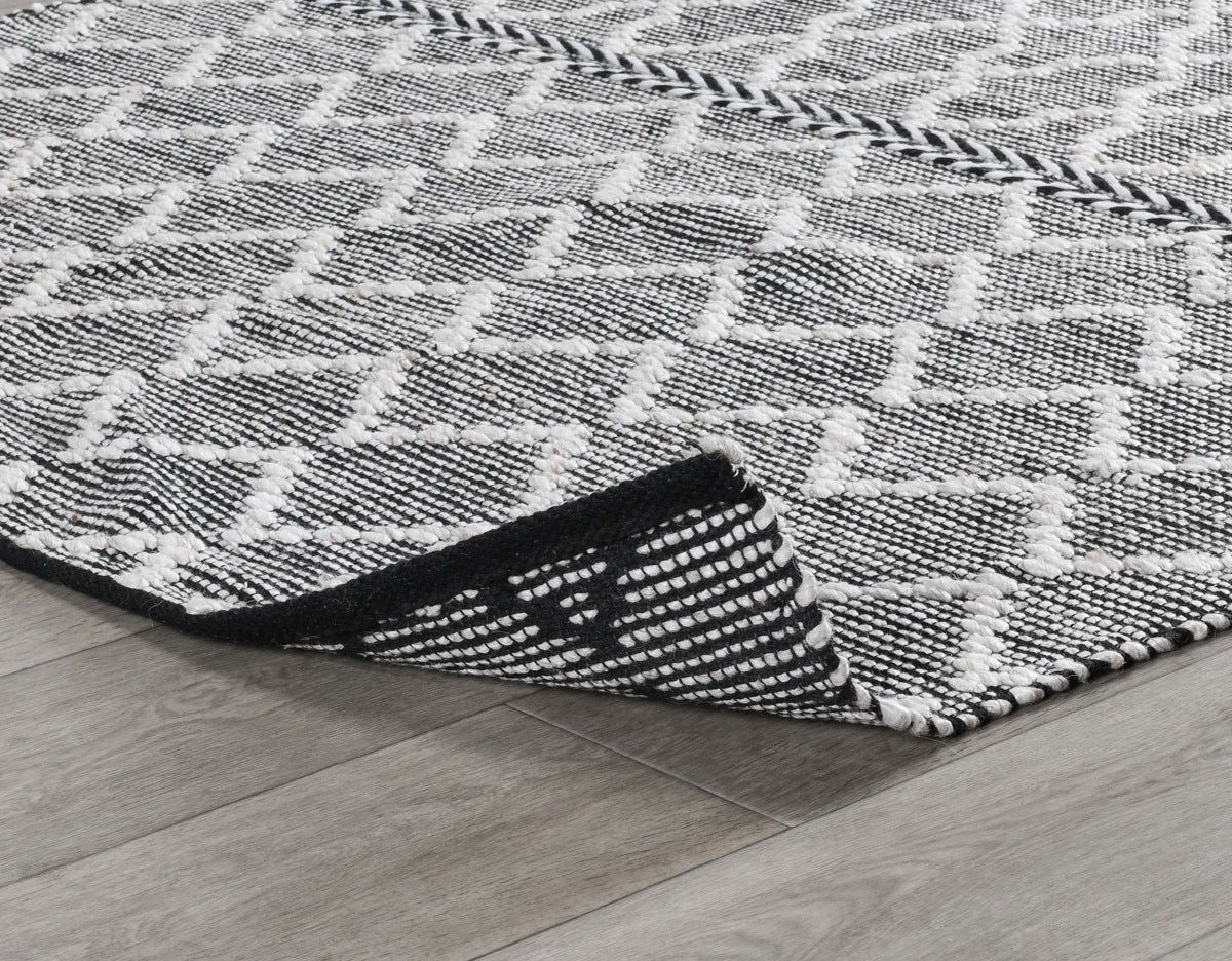 Black-and-white indoor/outdoor rug corner with textured geometric pattern and binding