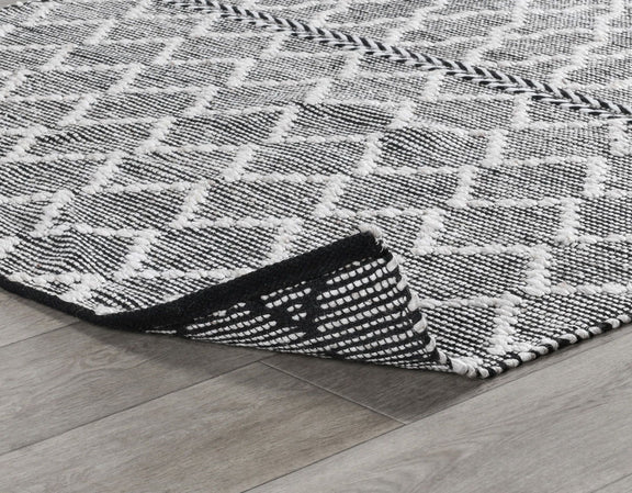 Black-and-white indoor/outdoor rug corner with textured geometric pattern and binding