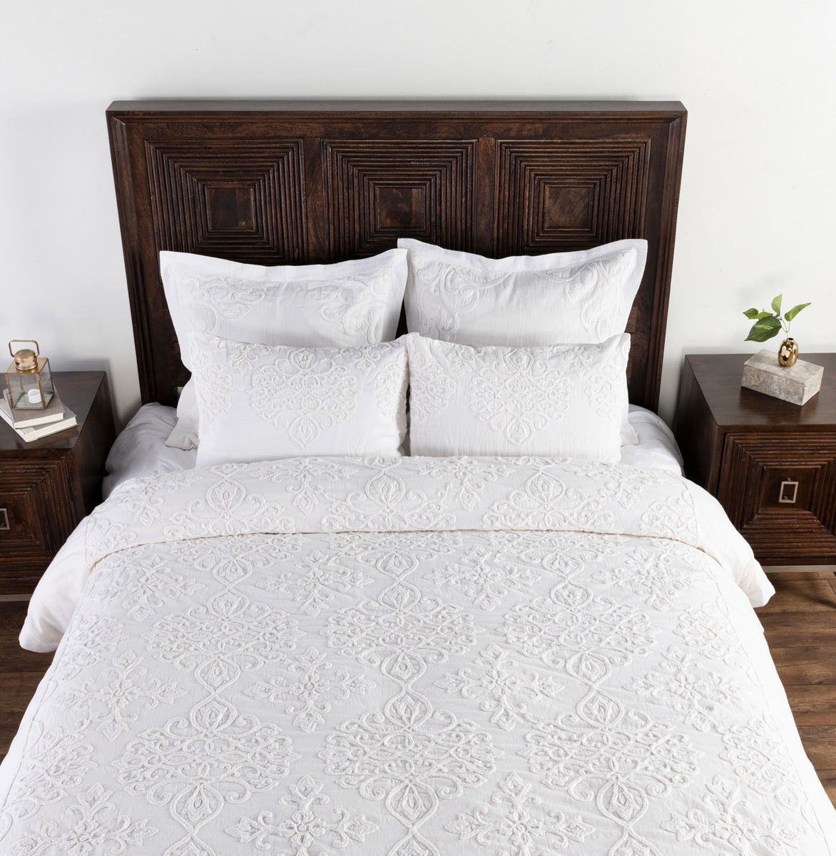 White embroidered duvet set with two shams on a dark wood upholstered headboard