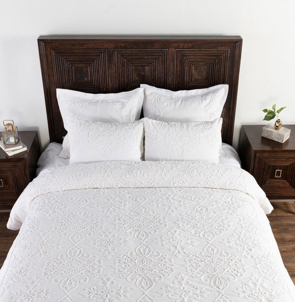 White embroidered duvet set with two shams on a dark wood upholstered headboard
