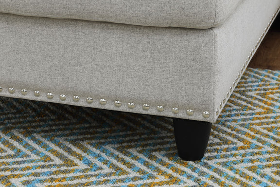 Gray sofa corner with nailhead trim and dark legs, shown over patterned rug