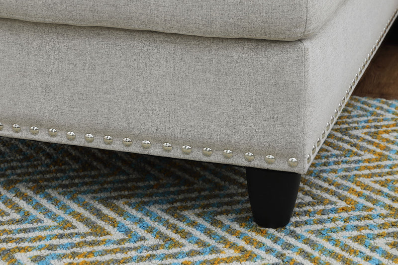Gray sofa corner with nailhead trim and dark legs, shown over patterned rug