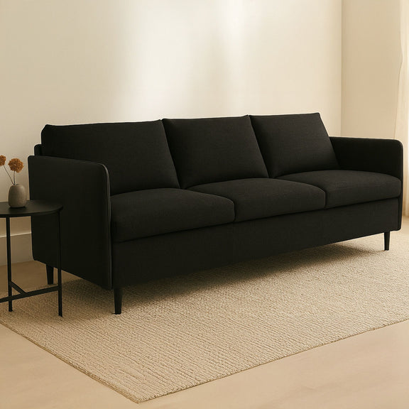 Dark warm black upholstered sofa with wide arms, three seat cushions, boxed back, tapered legs.