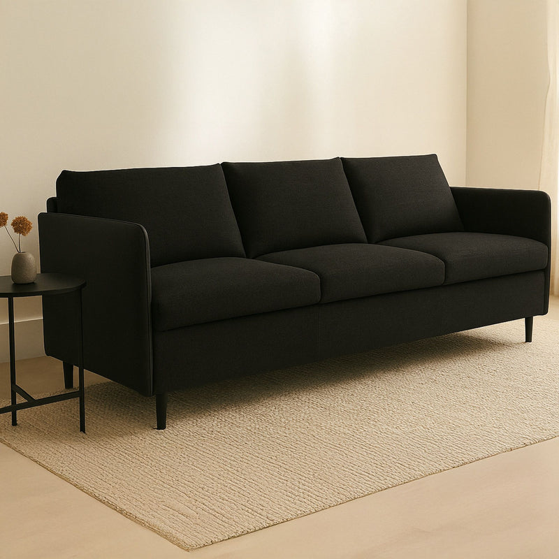Dark warm black upholstered sofa with wide arms, three seat cushions, boxed back, tapered legs.