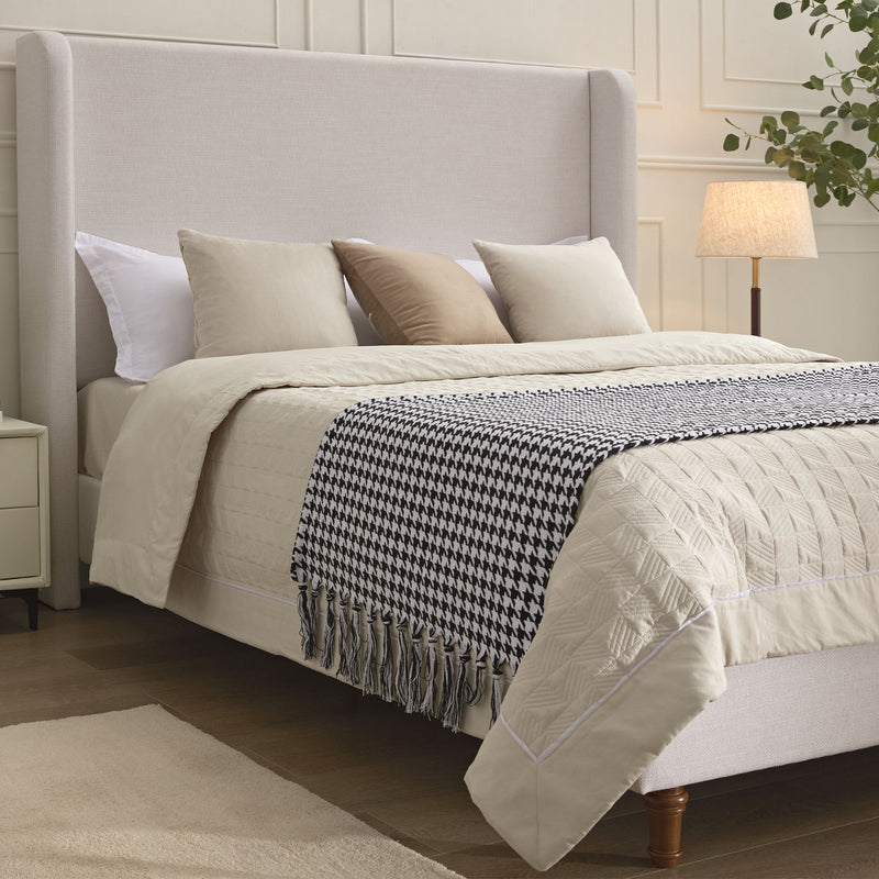 Angled view of ivory king bed with upholstered wingback headboard and wooden feet