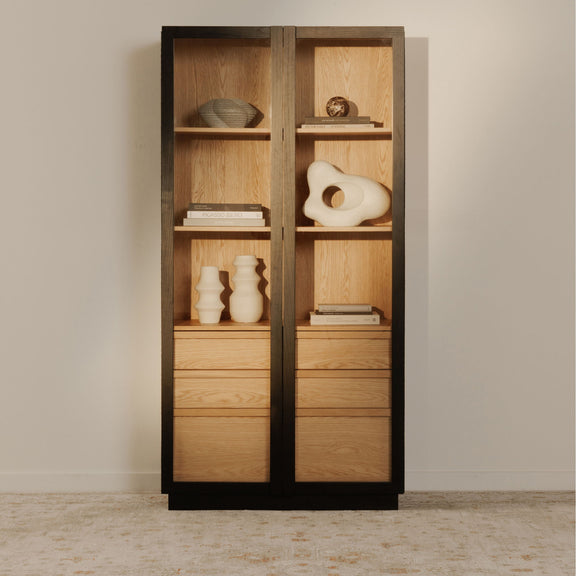 Tall cabinet with black frame, clear doors, and wood shelves with decor