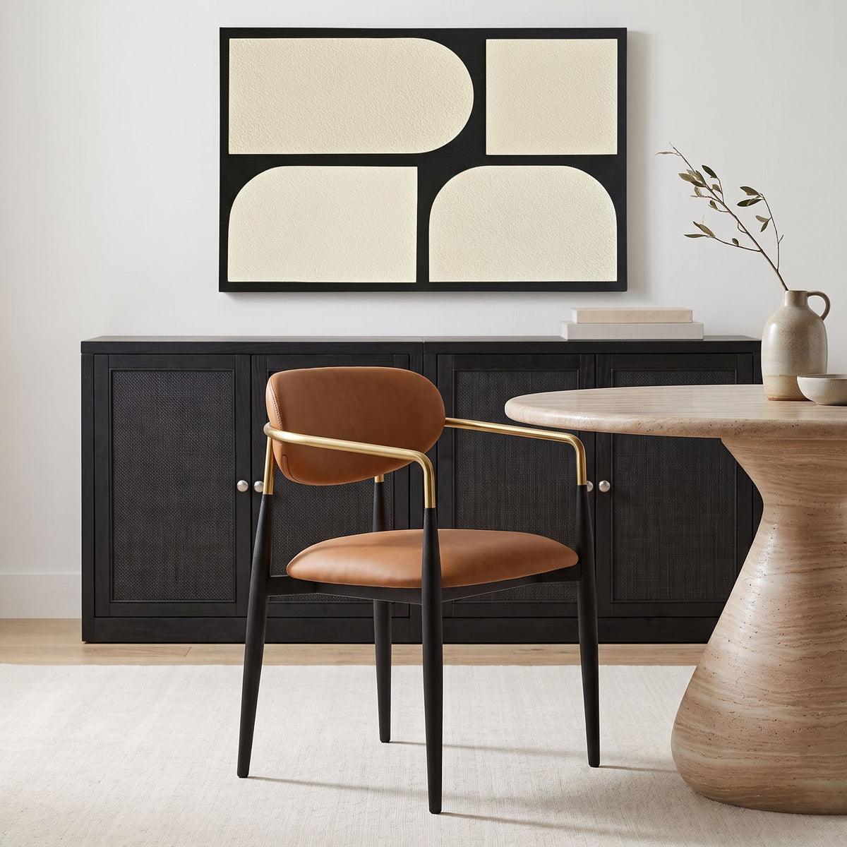 Tan upholstered dining arm chair with rounded back, black legs, gold arm frame