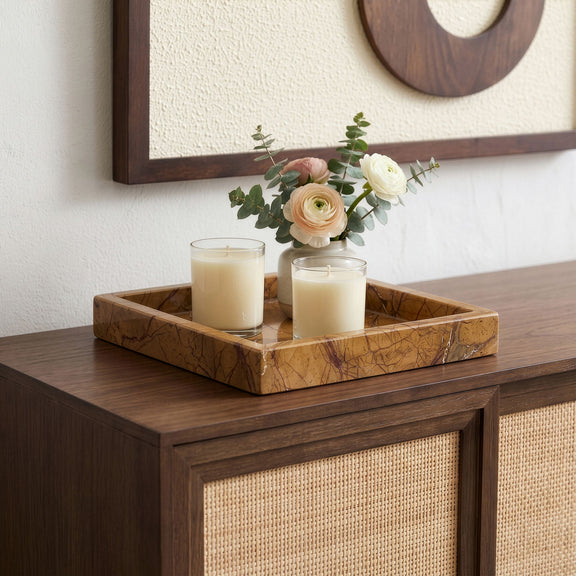 Tan marble tray with three white candles and a small floral arrangement.