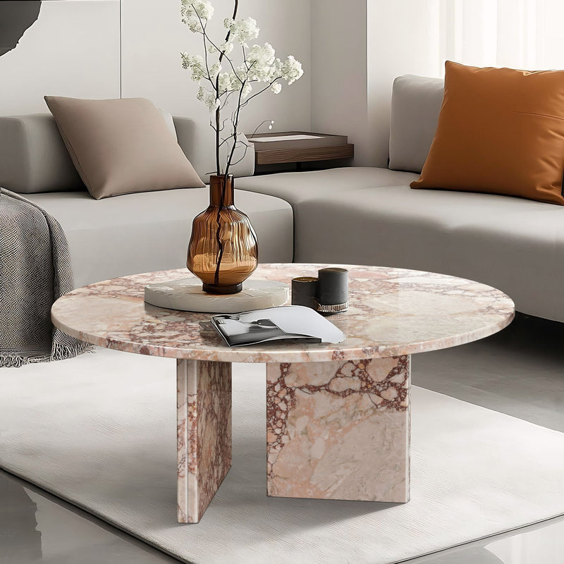 Round stone coffee table with light pink marble veining and thick cube base.