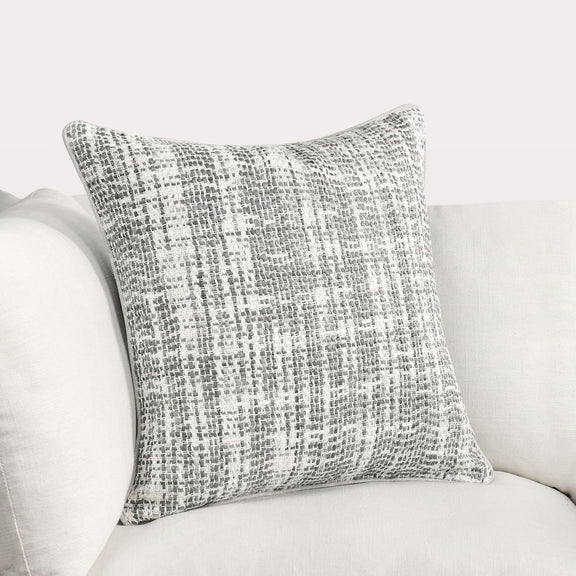 Light gray speckled woven throw pillow with piped edge on a sofa