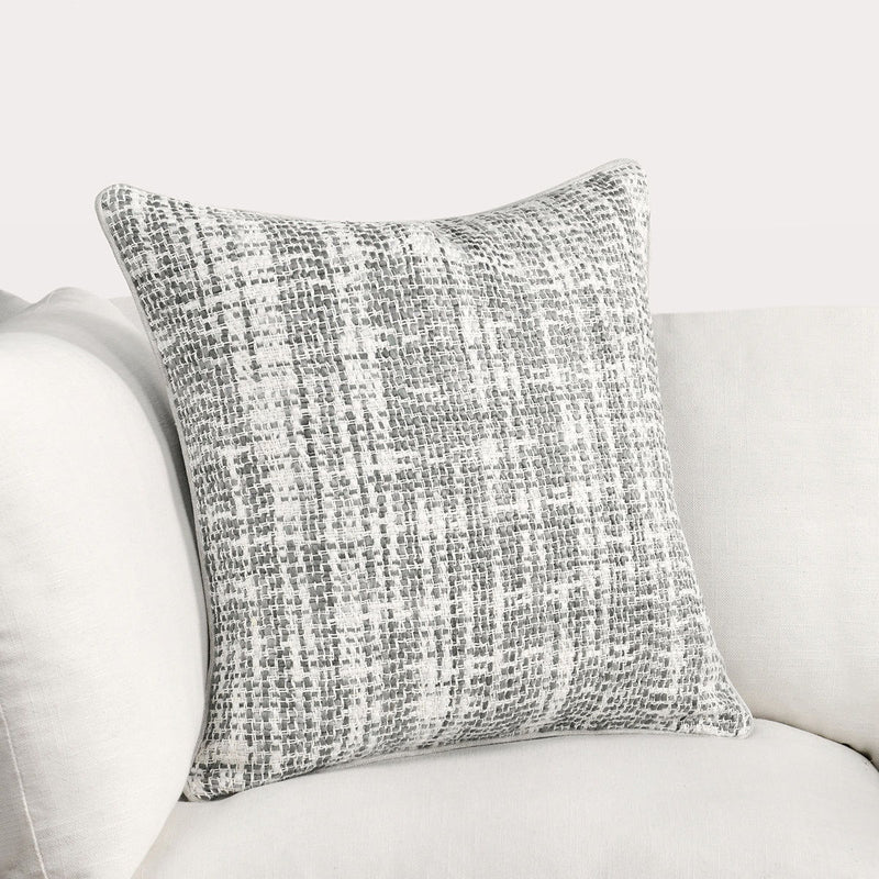 Light gray speckled woven throw pillow with piped edge on a sofa