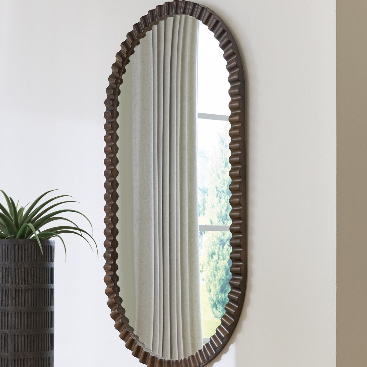 Oval wall mirror with ribbed dark brown frame and vertical reflection