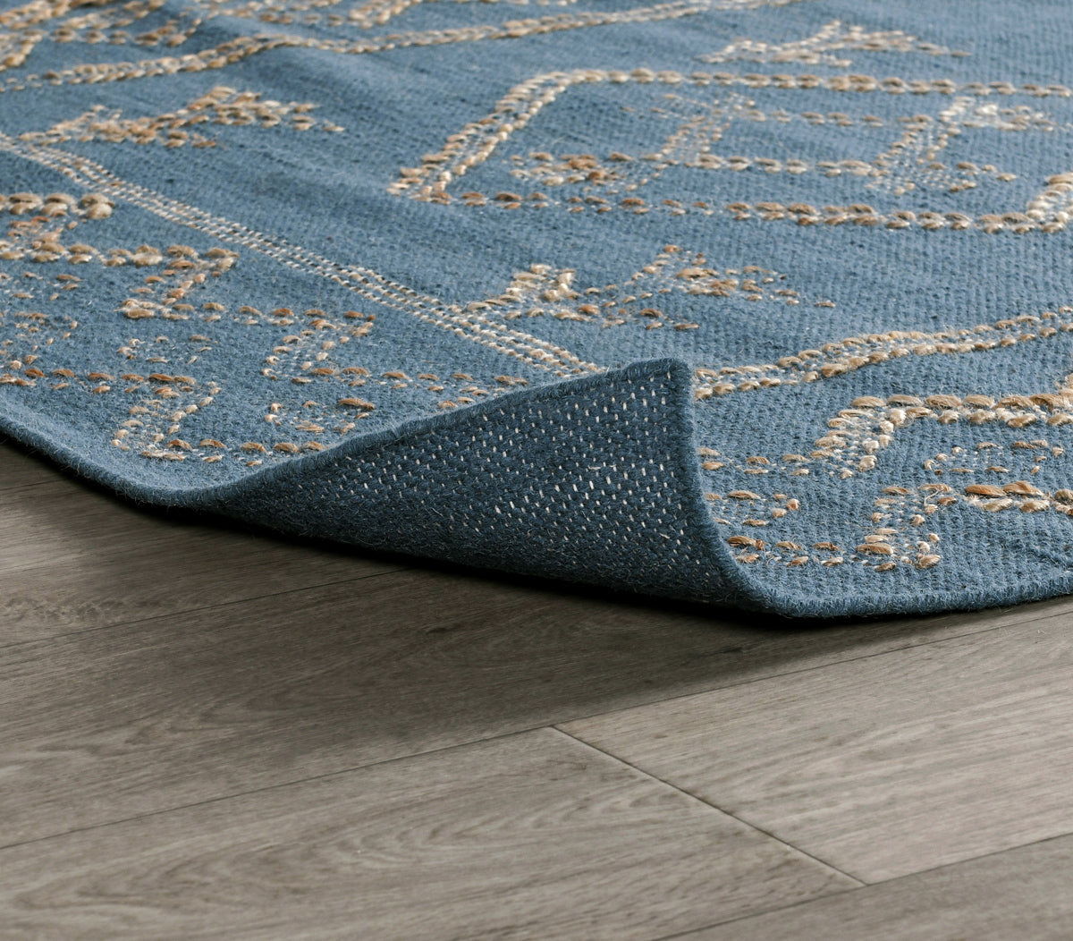 Blue rug corner close-up with stitched geometric border in gold on low pile