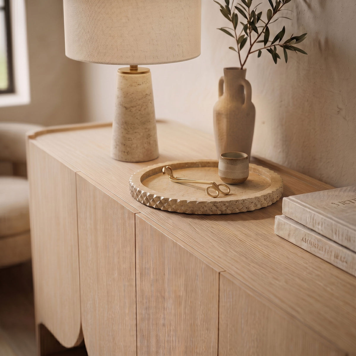 Beige travertine tray on wooden dresser holding small brass scissors and tools.