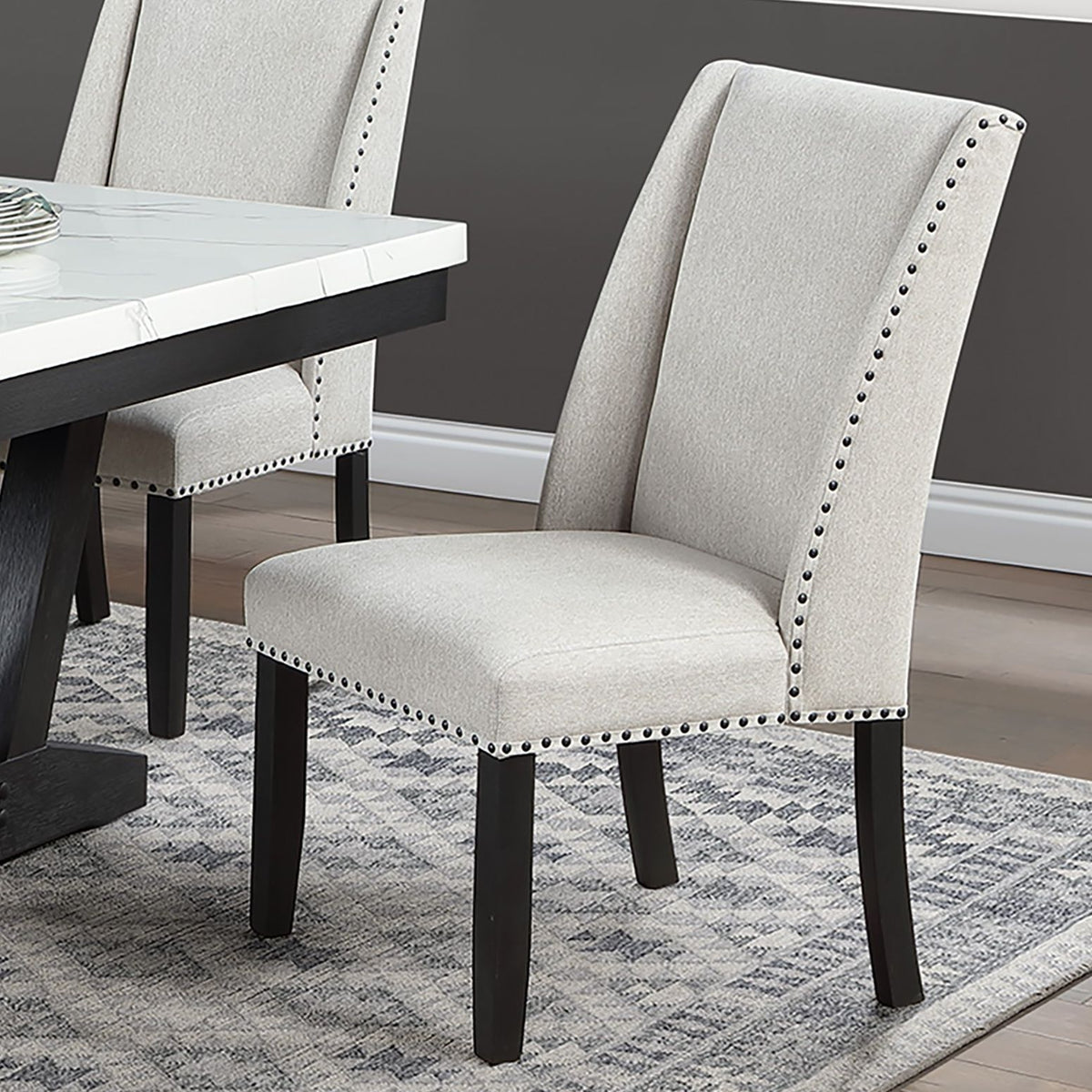 Wingback dining chair in light beige upholstery with nailhead trim and dark wooden legs